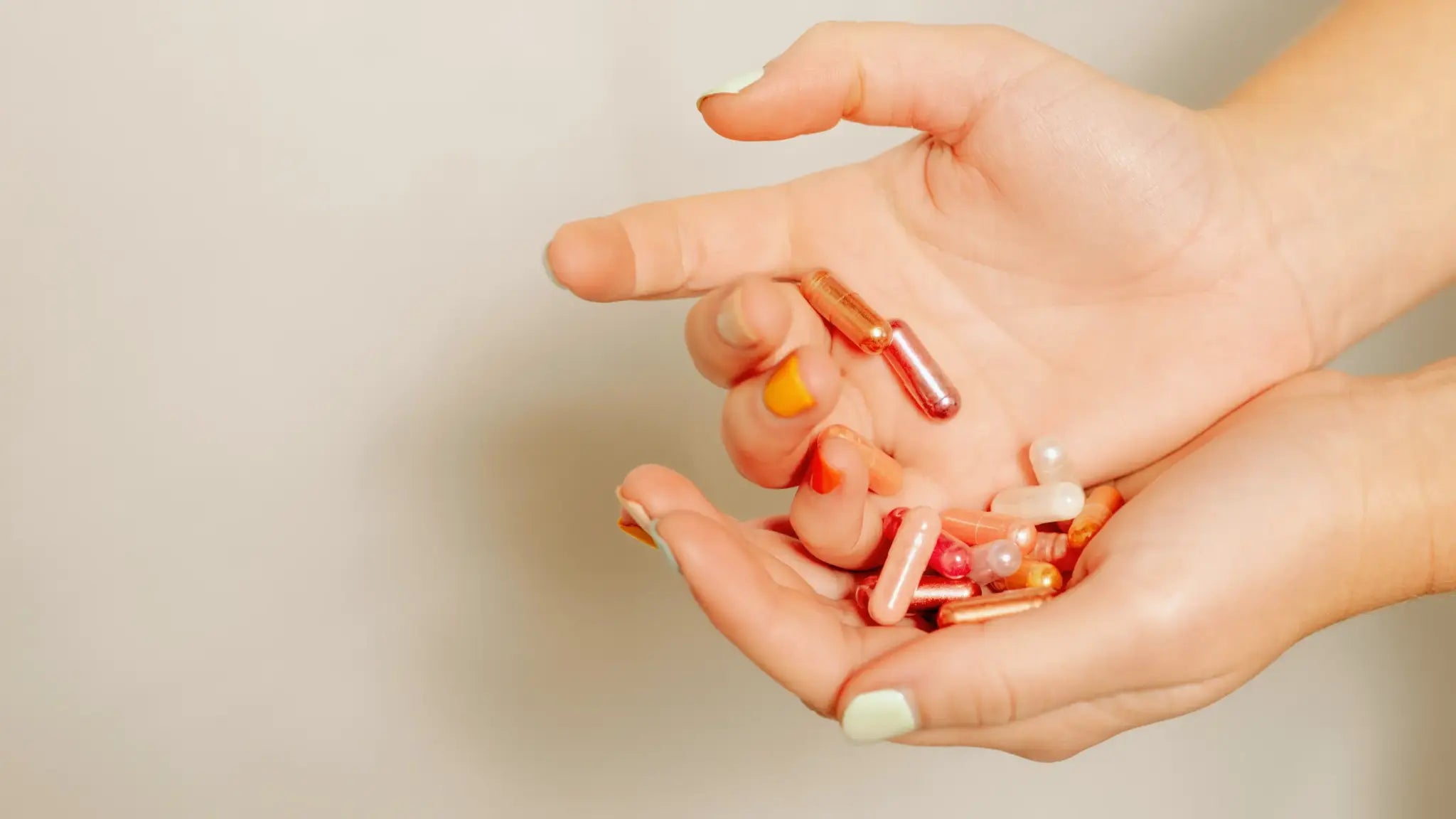 Close-up of hands holding pink and orange supplement capsules against a neutral background, illustrating TMG and NMN anti-aging supplements.