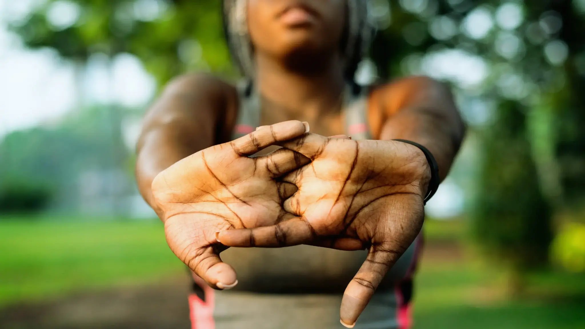 Close-up of a person outdoors stretching their clasped hands forward against a blurred green park background, symbolizing renewed energy and vitality for top NAD+ supplements.
