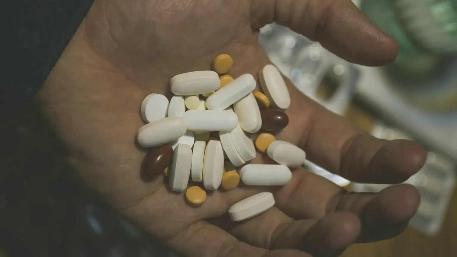 Close-up of an open palm holding a mix of white, yellow, and brown supplement capsules and tablets, illustrating Andrew Huberman’s recommended supplement list.